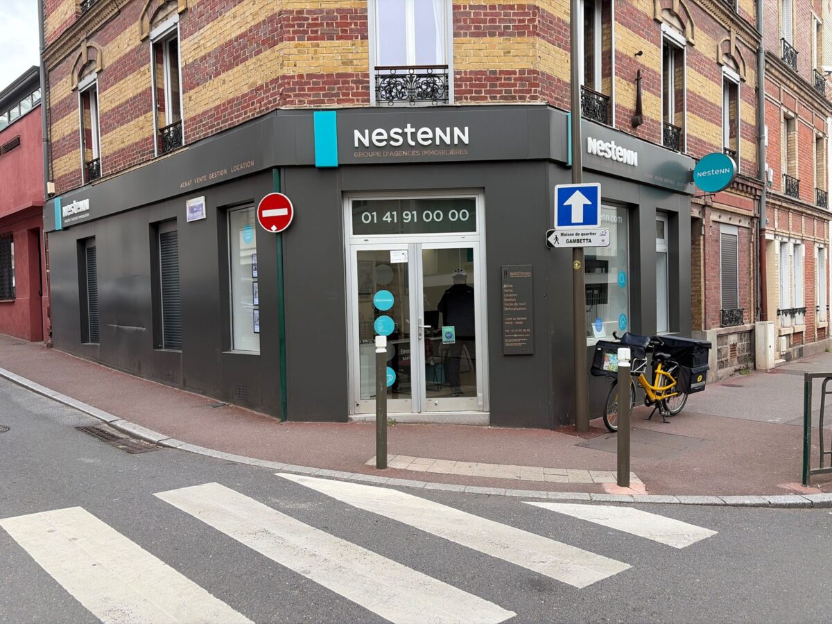 Façade d'une agence immobilière Nestenn avec vitrine d'annonces et panneau de vente
